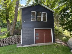 Dark gray shed with red garage door in a grassy wooded yard