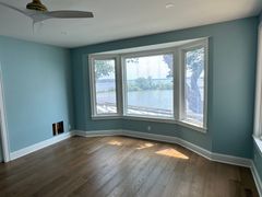 Empty light-blue room with a bay window, wood floors, and sunlight streaming in