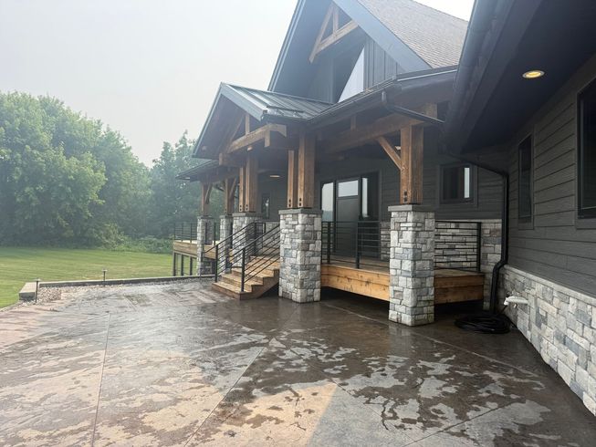 Rustic log cabin interior with stone fireplace, wood-paneled walls, and a kitchen visible through an opening