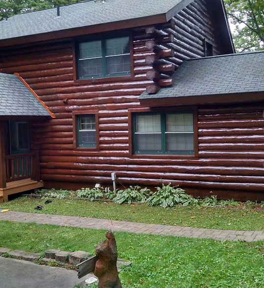 Log cabin exterior with windows, gray roof, and a small dog in the foreground on a grassy lawn.
