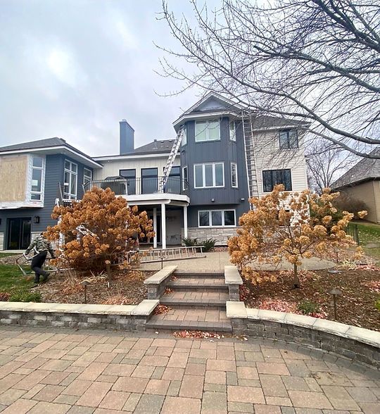 Large gray stone house with front steps, brick driveway, and bare trees in winter