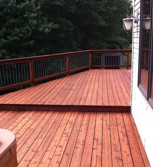 Large red wooden deck with railings beside a house, overlooking trees