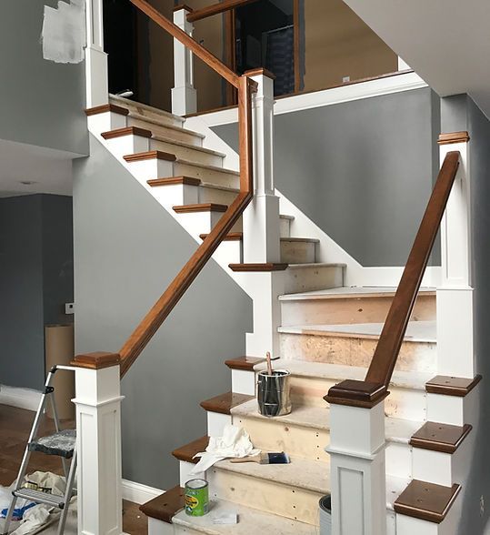 Interior staircase with white walls, wood handrails, and partially unfinished steps and supplies on the landing.