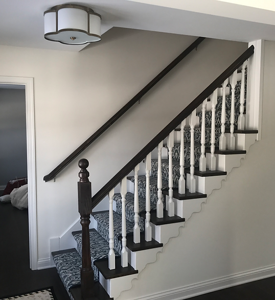 Interior staircase with black railings, white balusters, and dark carpeted steps in a home.