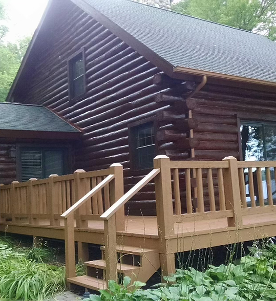 Log cabin with a wooden front porch and steps surrounded by greenery