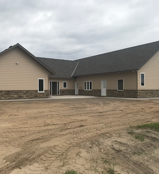 Single-story beige house under construction with stone accents and a dirt lot in front