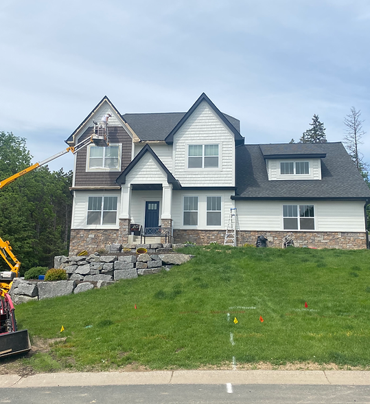 Two-story white and gray house with stone landscaping and a green front lawn under a cloudy sky