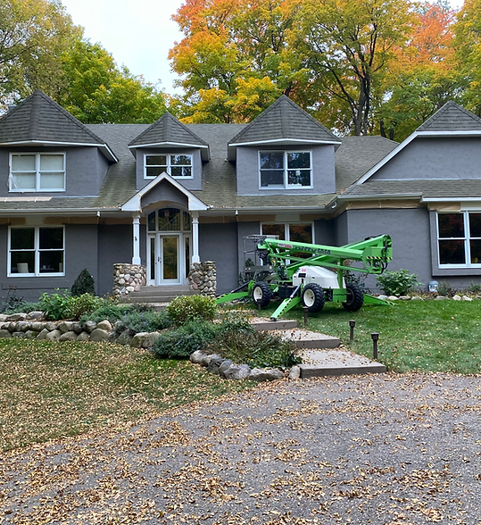 Gray suburban house with autumn trees and a green boom lift parked in the front yard