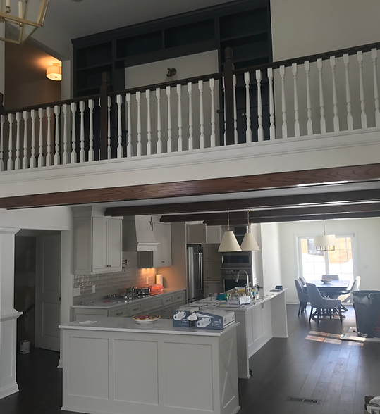 Open-plan kitchen and dining room with a loft railing and white cabinets, viewed from below.