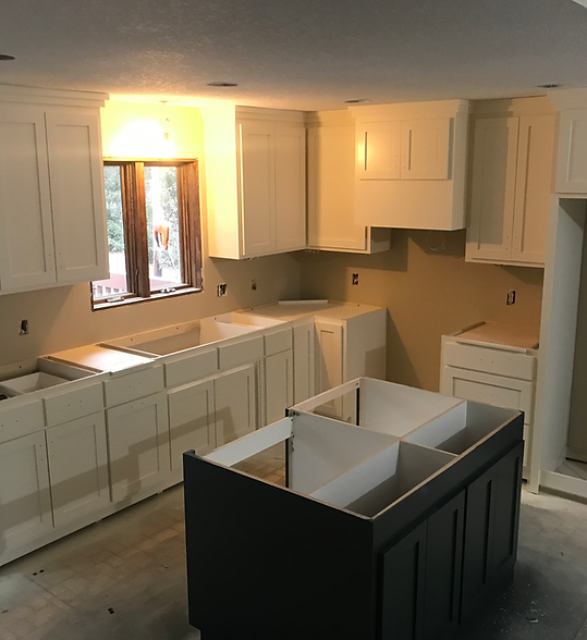 Kitchen under renovation with white cabinets and a dark island cabinet in the center
