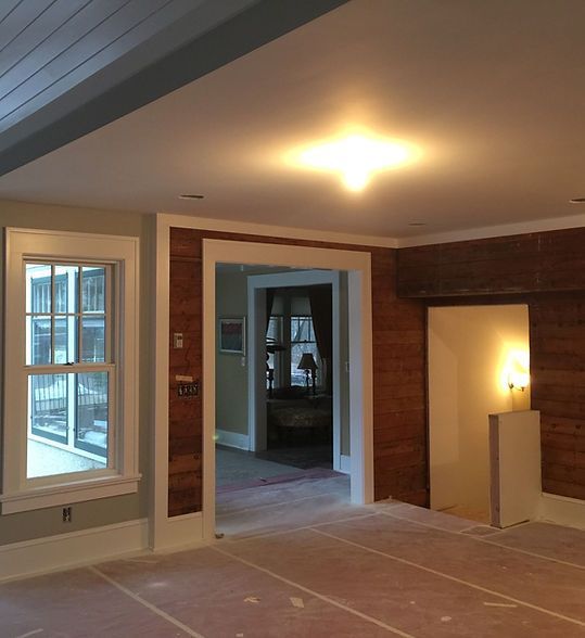 Empty room under renovation with bare floors, brick accents, and a doorway to another room