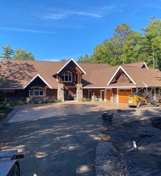 Large rustic house with brown roof, stone entry, and a driveway in front under a clear blue sky