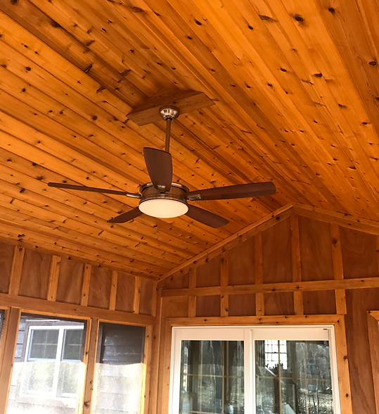 Wood-paneled porch ceiling with a dark ceiling fan and windows below