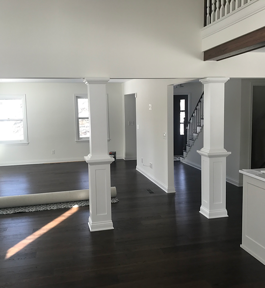 Empty modern living room with dark hardwood floors, white columns, and staircase in background