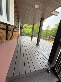 Covered wooden porch with dark posts, white railings, and green trees beyond.