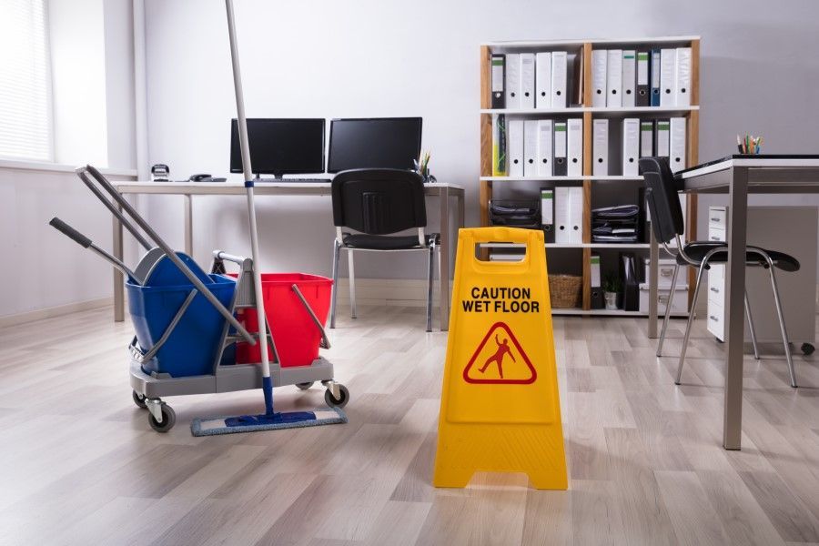 A caution wet floor sign is in an office next to a mop and buckets.