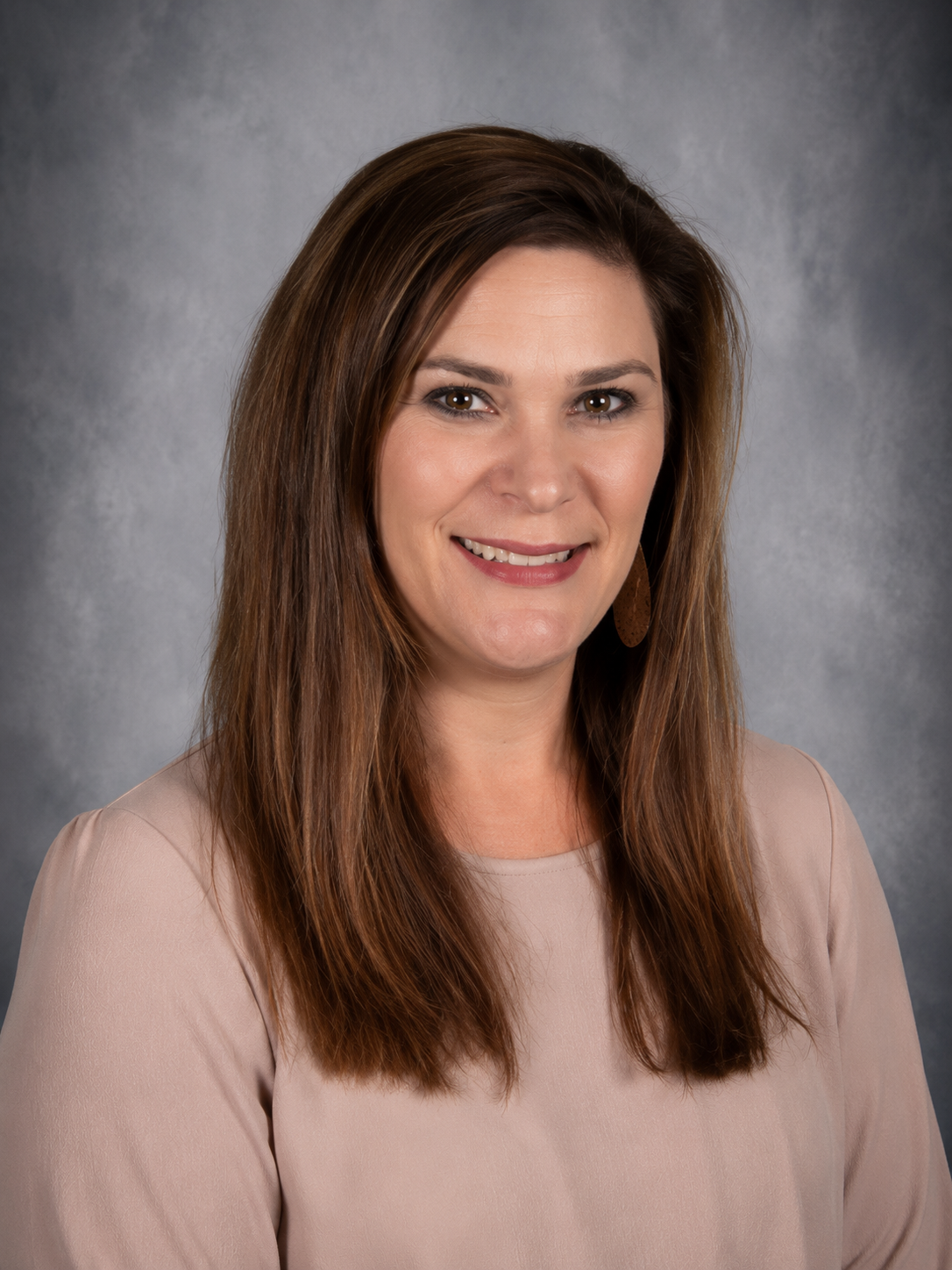 Woman with brown hair, smiling, wearing a sweater, against a mottled gray background.