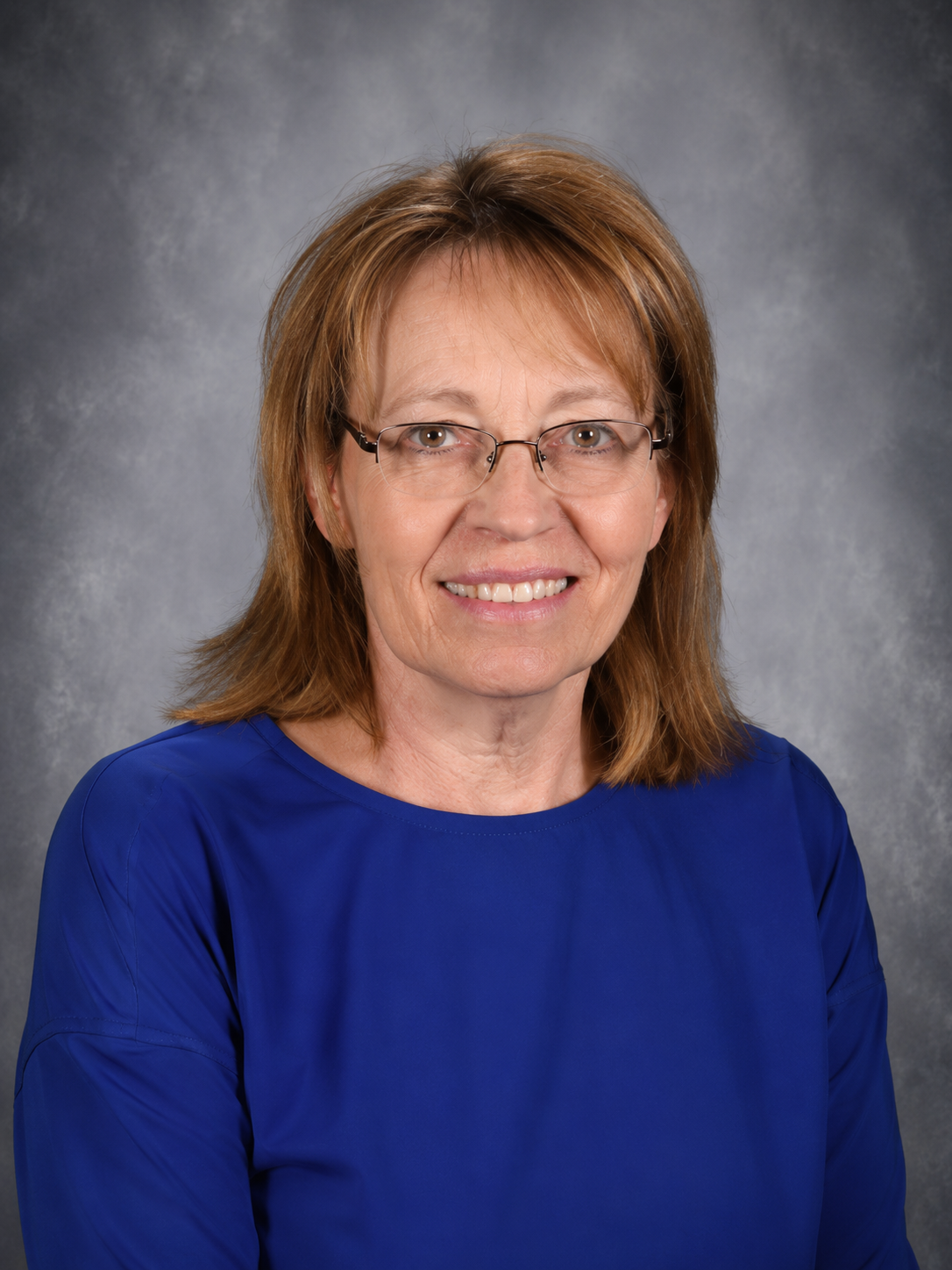 Woman with glasses, smiling, in a red sweater, against a blurred background.