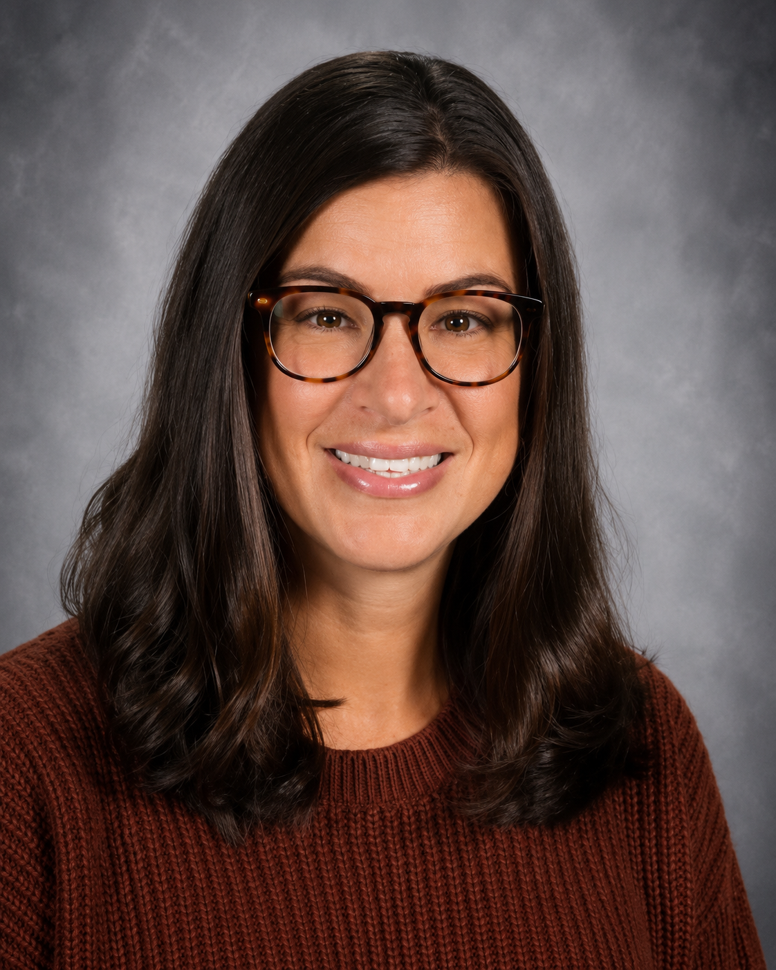 Woman with glasses, smiling, in a red sweater, against a blurred background.