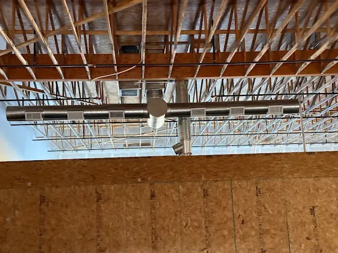 View of a building's wooden framing and ventilation system suspended from the ceiling.