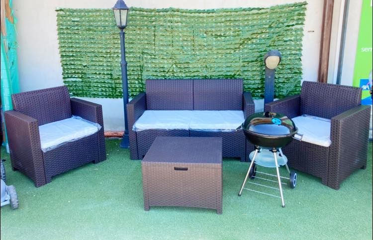 Set di mobili da esterno per patio: divano, due sedie, tavolo e barbecue su tappeto verde.
