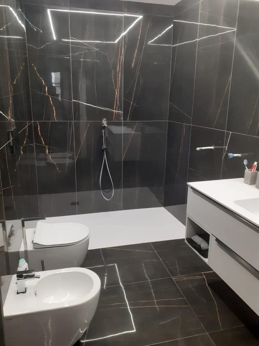 Moderno bagno in marmo nero con cabina doccia, WC, bidet e mobile lavabo sospeso.