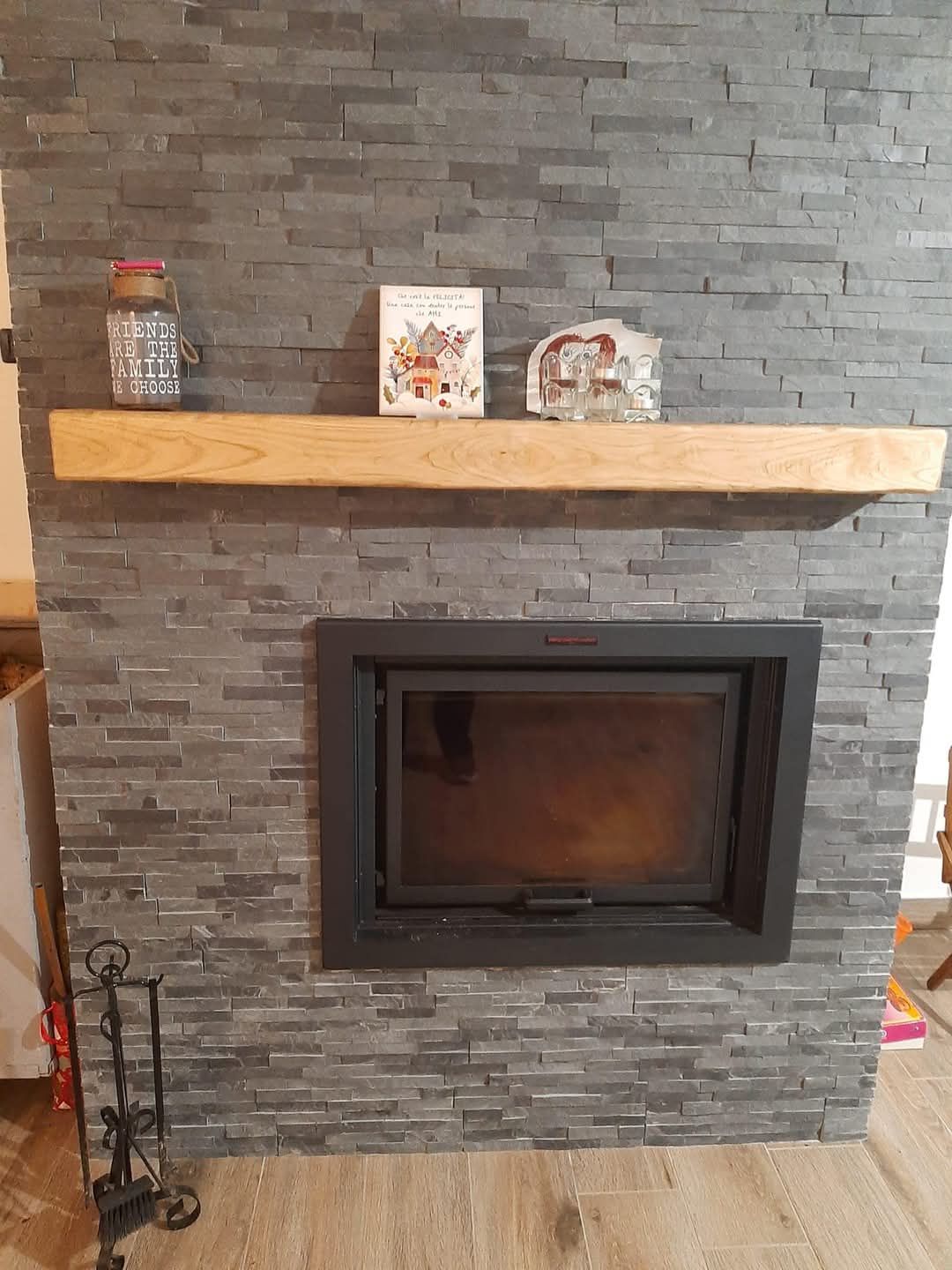 Camino con cornice in pietra grigio scuro, mensola in legno e oggetti decorativi.