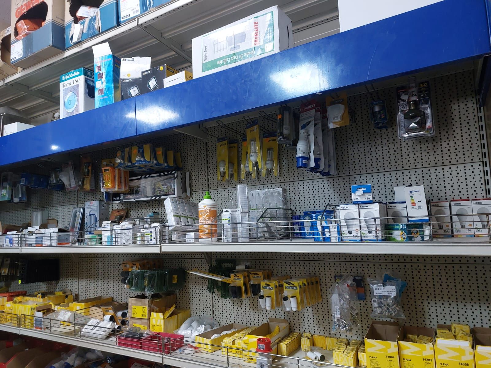 Scaffali pieni di materiale di ferramenta in un negozio, tra cui utensili, componenti elettrici e vari articoli confezionati.