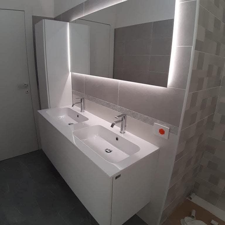 Moderno mobile da bagno bianco con due lavandini, un grande specchio retroilluminato e un mobile alto.