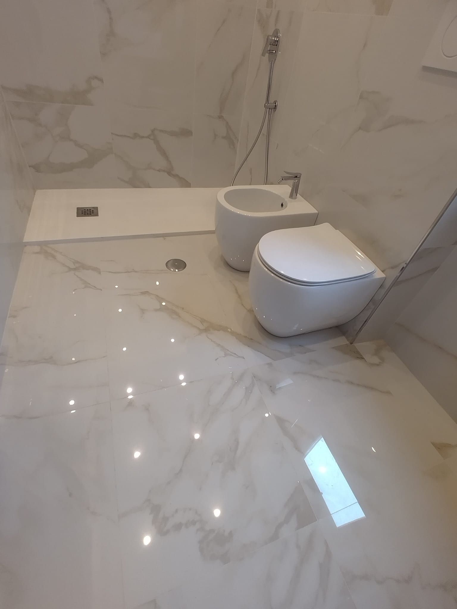 Bagno in marmo bianco con WC, bidet e zona doccia. Pavimento e pareti lucidi.