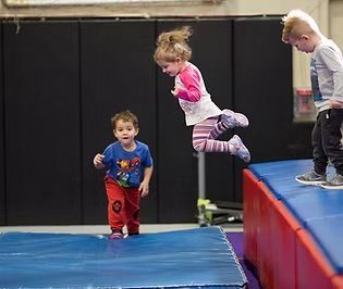 Children jumping and playing on mats in a gym. One child leaps, others watch.