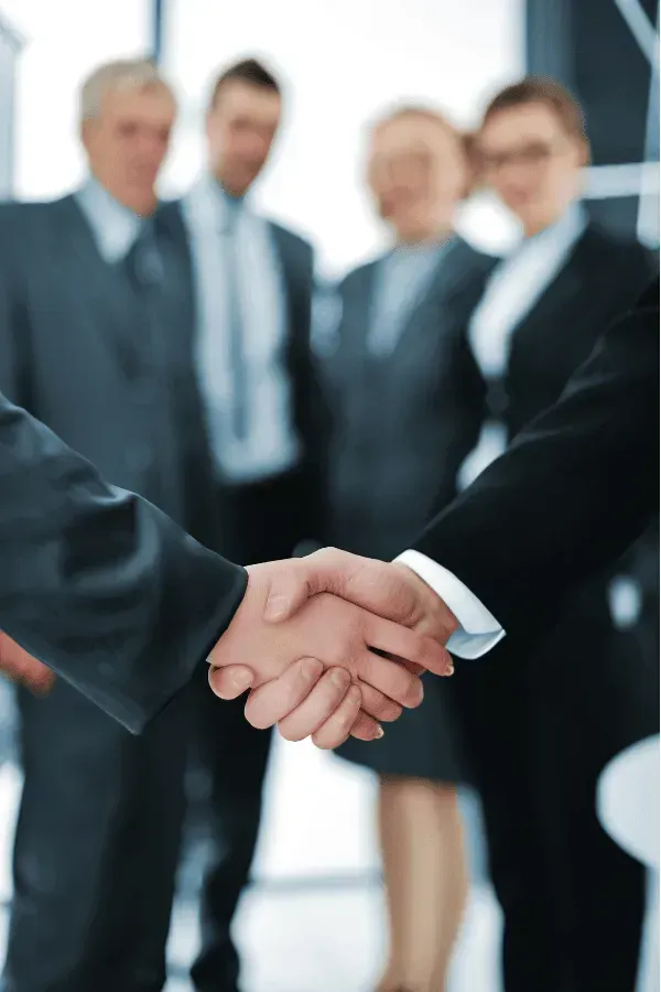 Um homem e uma mulher apertando as mãos na frente de um grupo de empresários