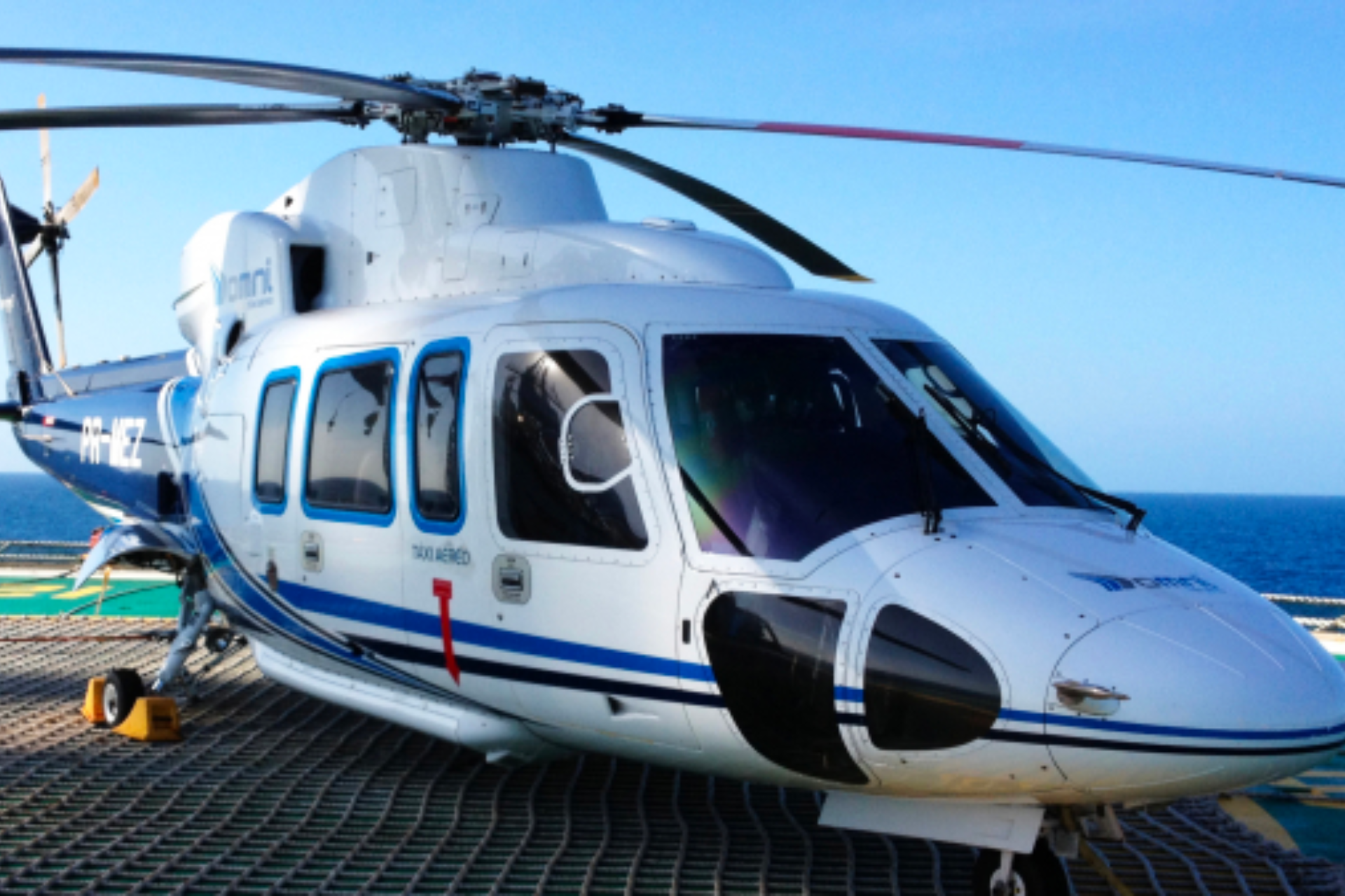 Um helicóptero branco e azul está estacionado em uma pista perto do oceano