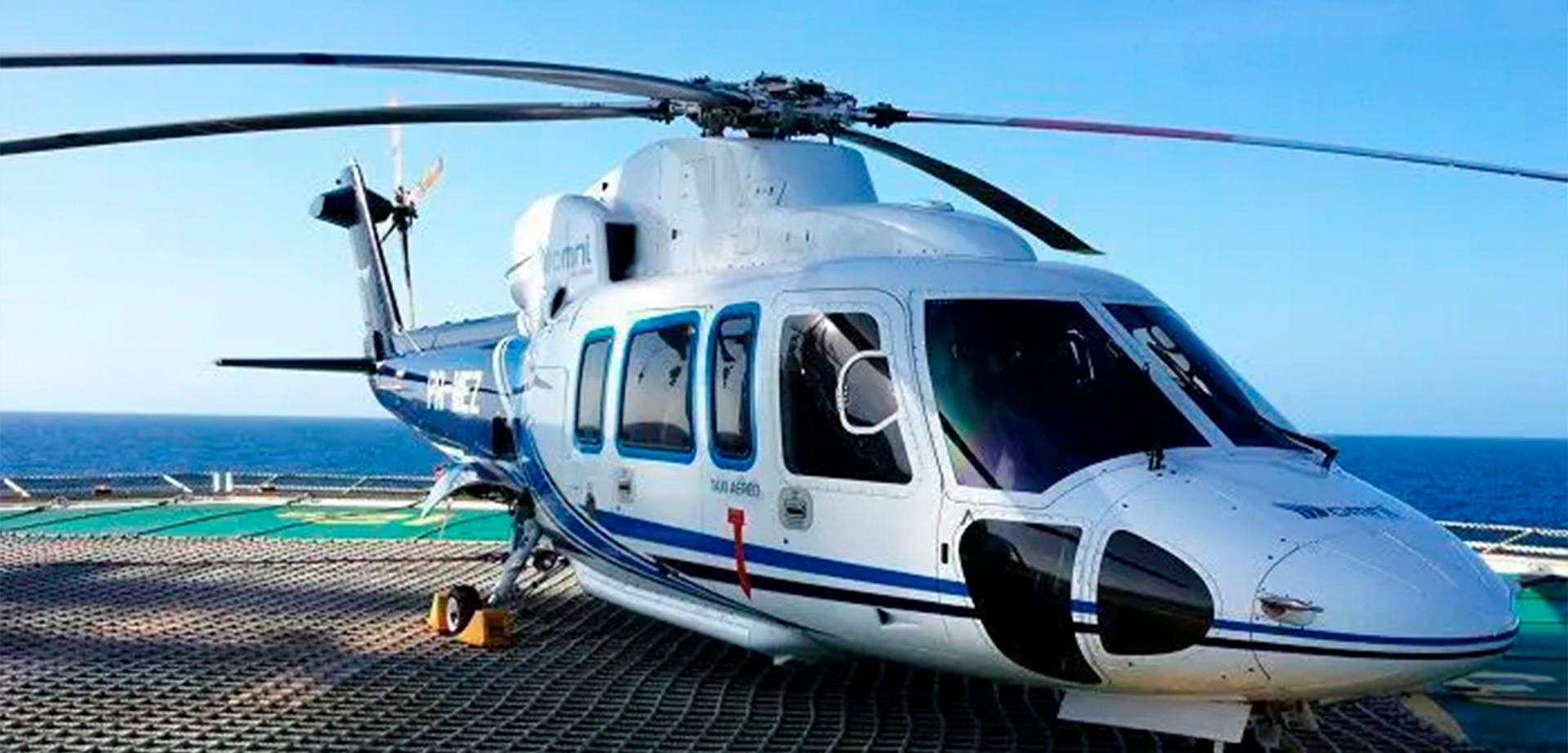 Um helicóptero branco e azul está estacionado em uma pista perto do oceano.