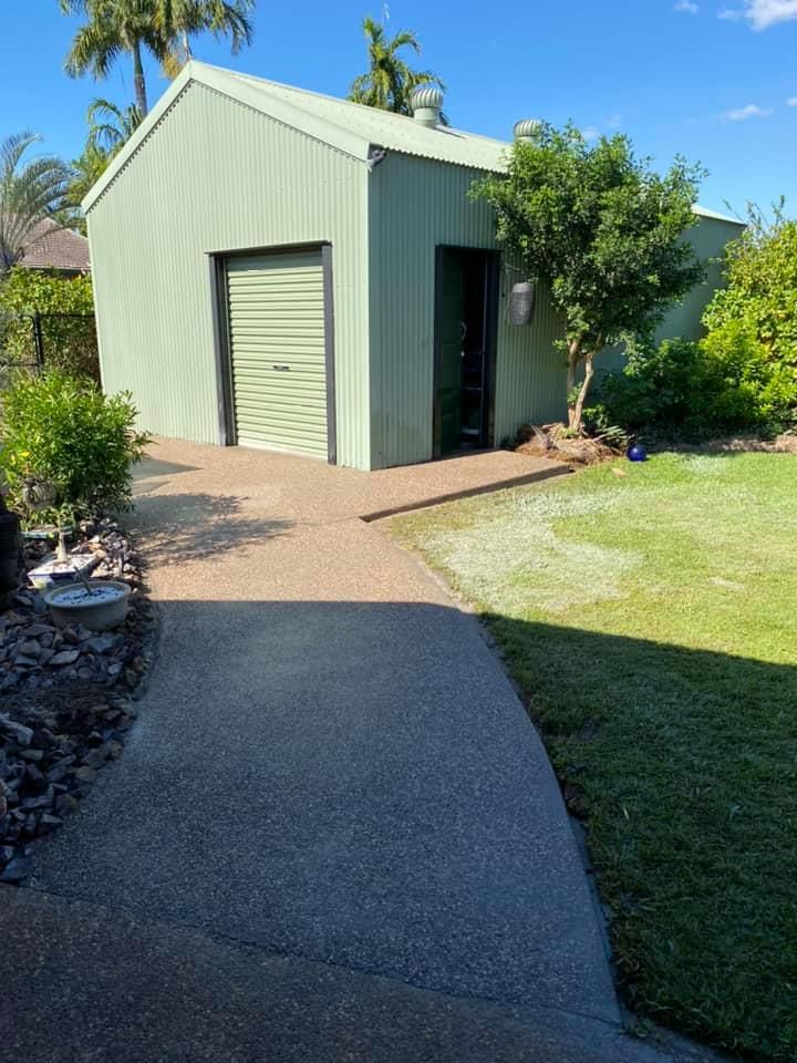 Green metal shed with a roller door and side door, on a concrete path and lawn, against a blue sky — Dwayne Hamlyn Concreting in Woodroffe, NT