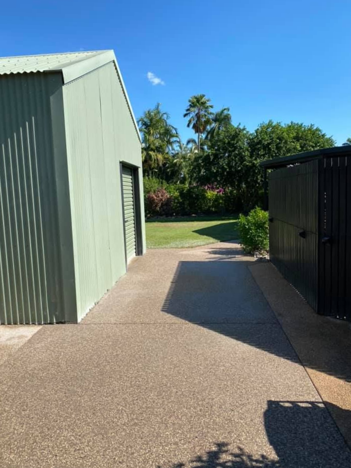 Concrete path between two buildings, one green, one black. Backyard, blue sky, trees — Dwayne Hamlyn Concreting in Woodroffe, NT
