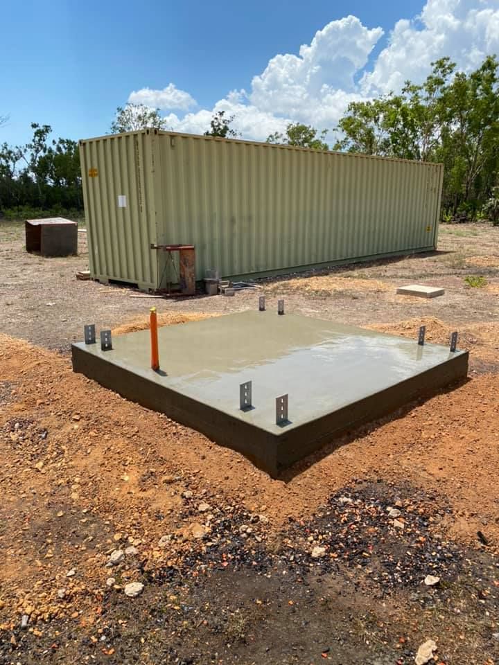 Freshly poured concrete foundation with anchor bolts in front of a shipping container — Dwayne Hamlyn Concreting in Woodroffe, NT