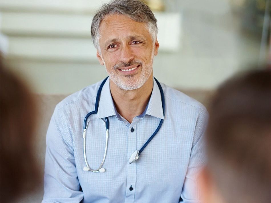 A doctor with a stethoscope around his neck is smiling while talking to a patient.