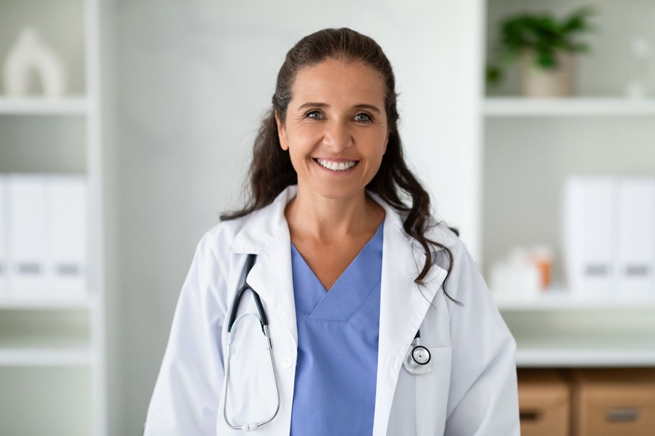 A female doctor with a stethoscope around her neck is smiling for the camera.