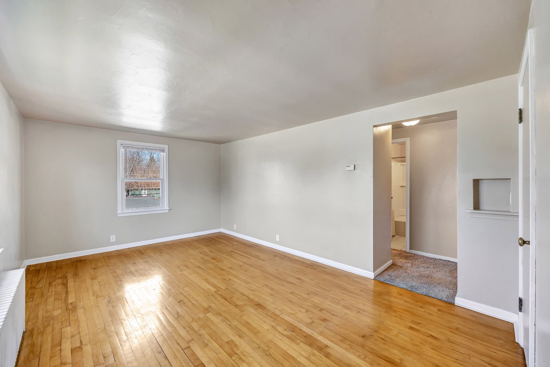 An empty living room with hardwood floors and white walls.
