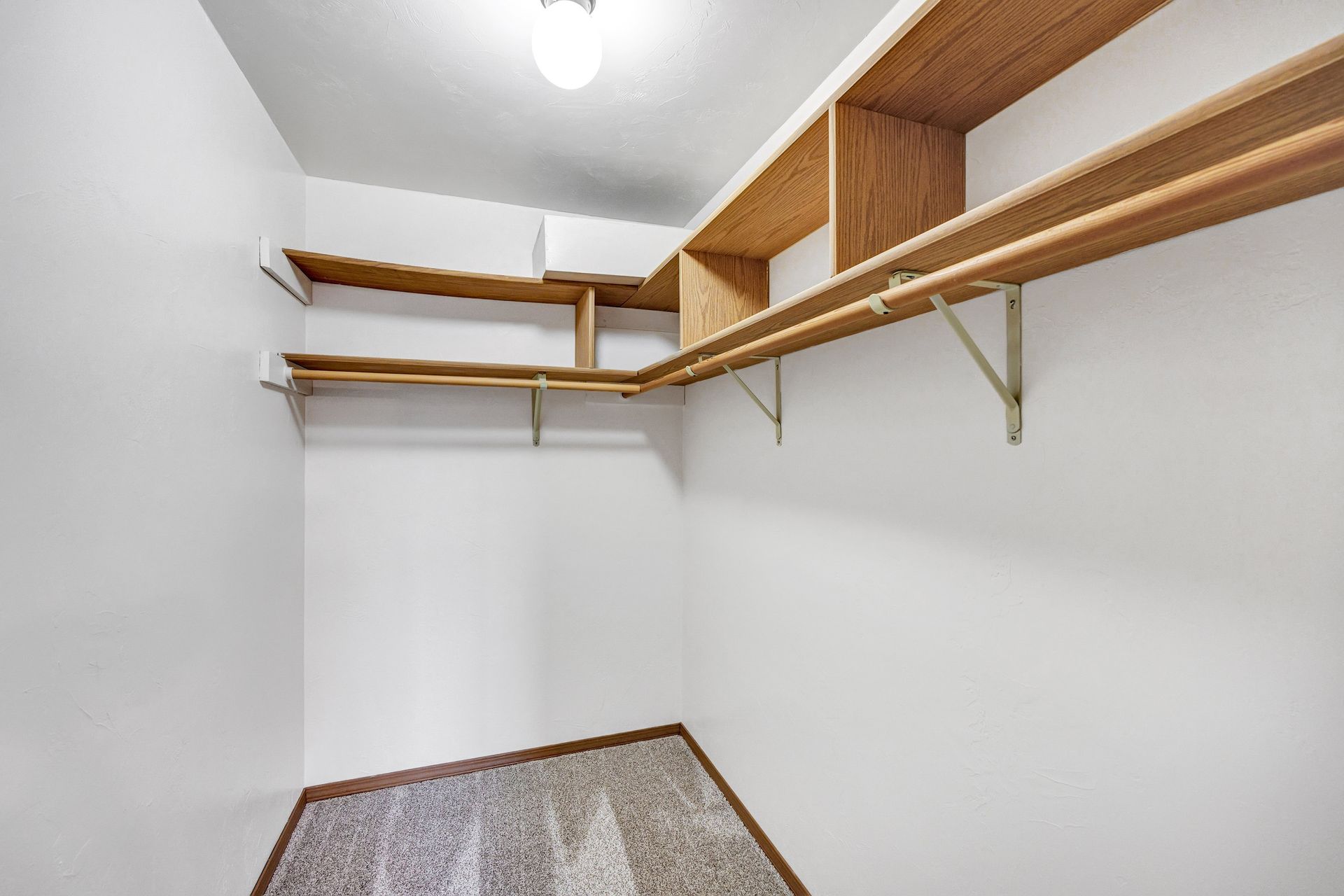 An empty walk in closet with wooden shelves and hanging racks.