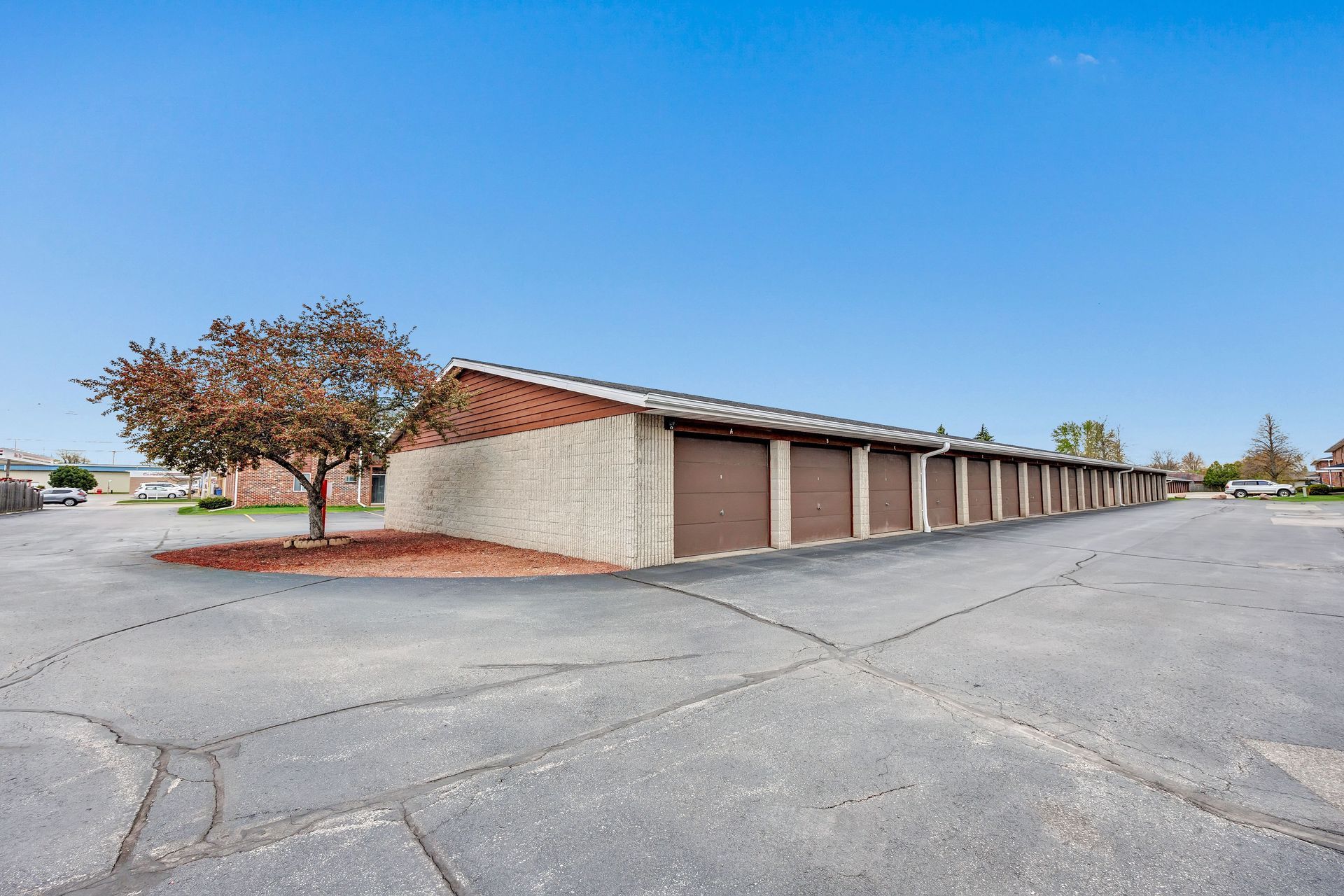 A row of garages with a tree in front of them in a parking lot.