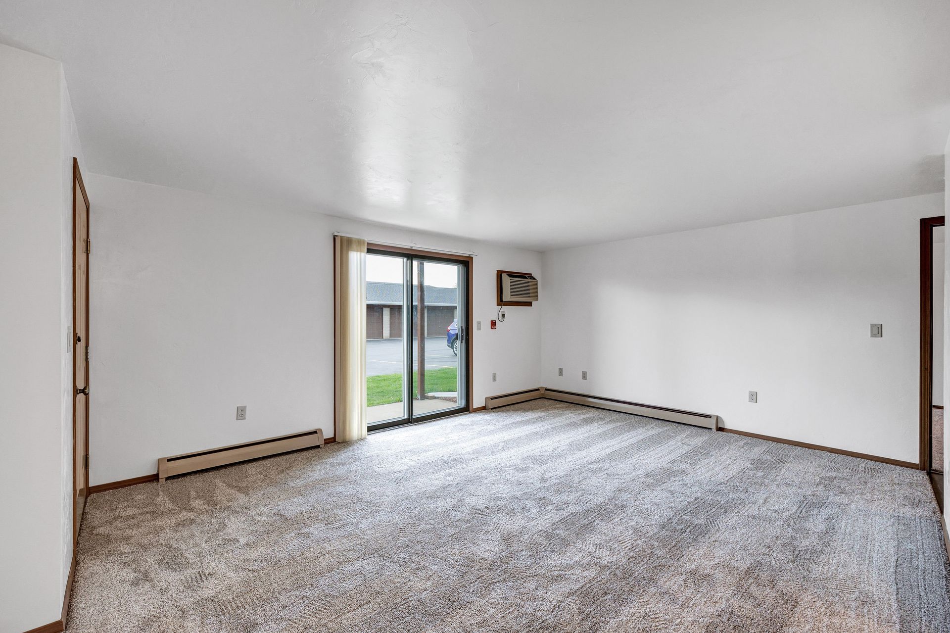 An empty living room with a sliding glass door and a carpeted floor.