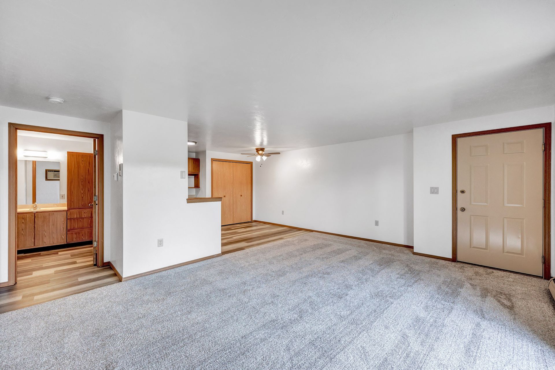 An empty living room with a carpeted floor and a ceiling fan.