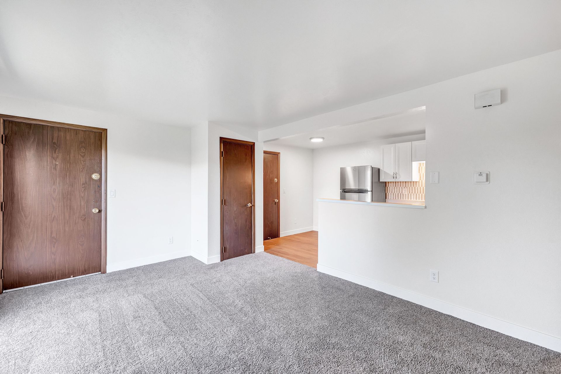 An empty living room with a gray carpet and white walls.