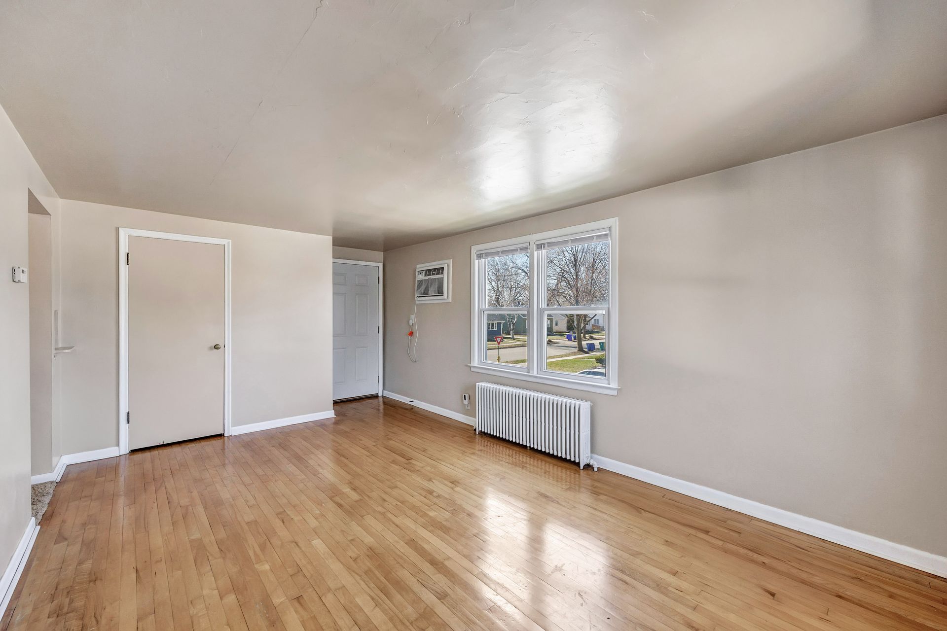 An empty living room with hardwood floors and two windows.