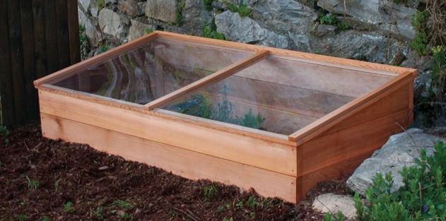 A closed cold frame consisting of wood sides and a glass top. It sits on the ground and is angled a bit towards the sun.