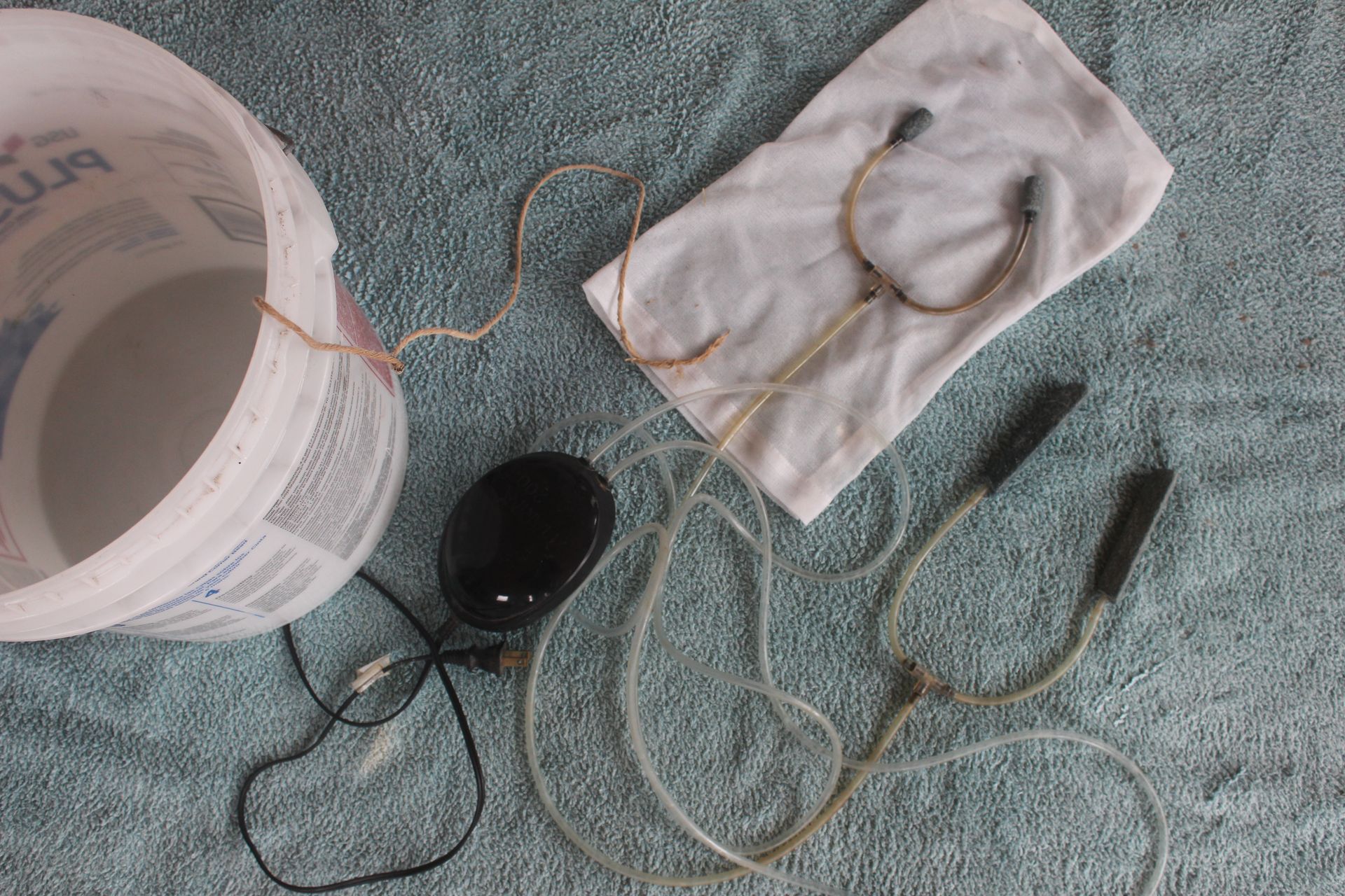 Equipment needed for making compost tea including five gallon bucket, an aquarium pump, hose and stones plus a net bag for the compost