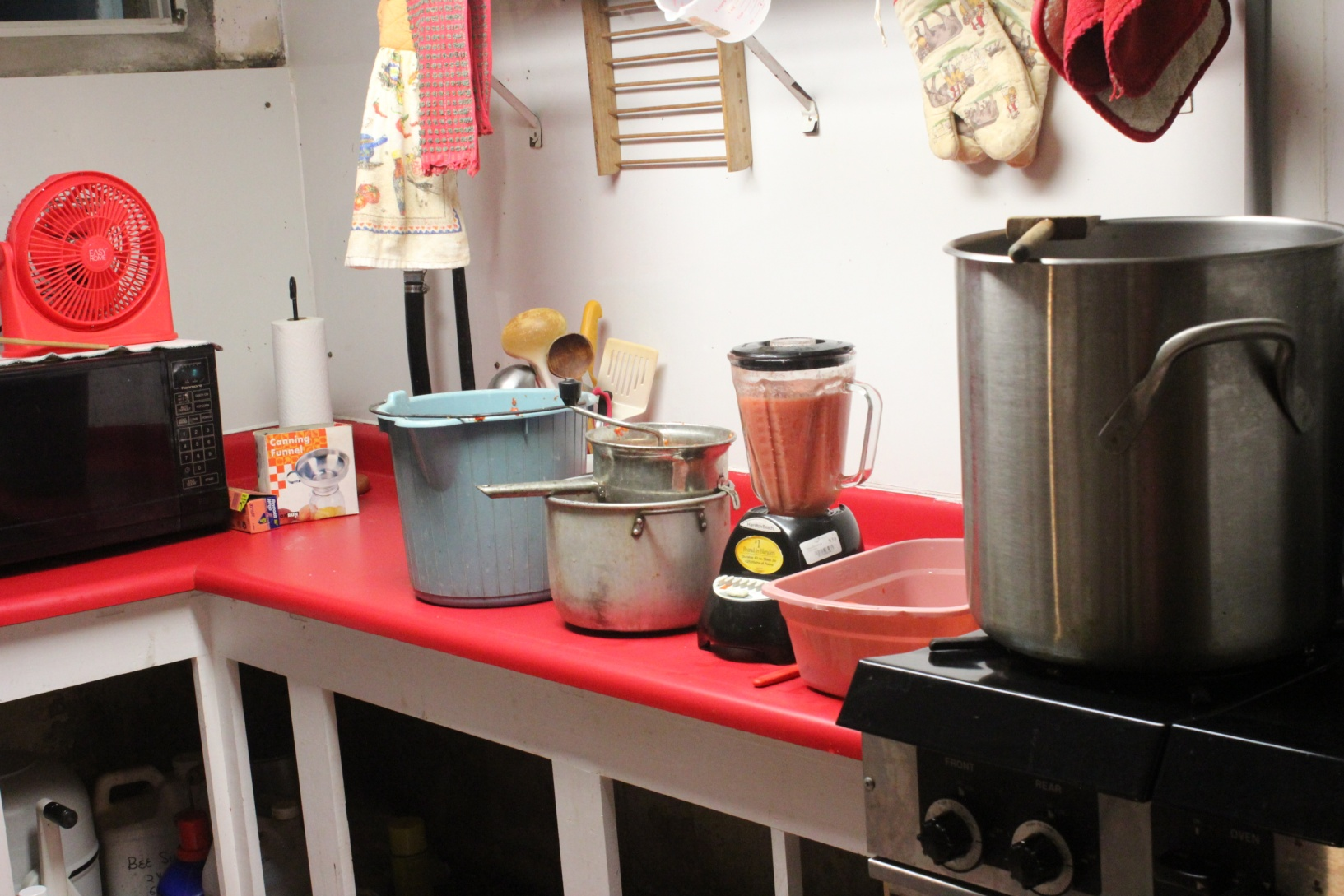 Photo of canning set-up including microwave, bucket for scraps, a food mill and large stainless steel pot of the stove