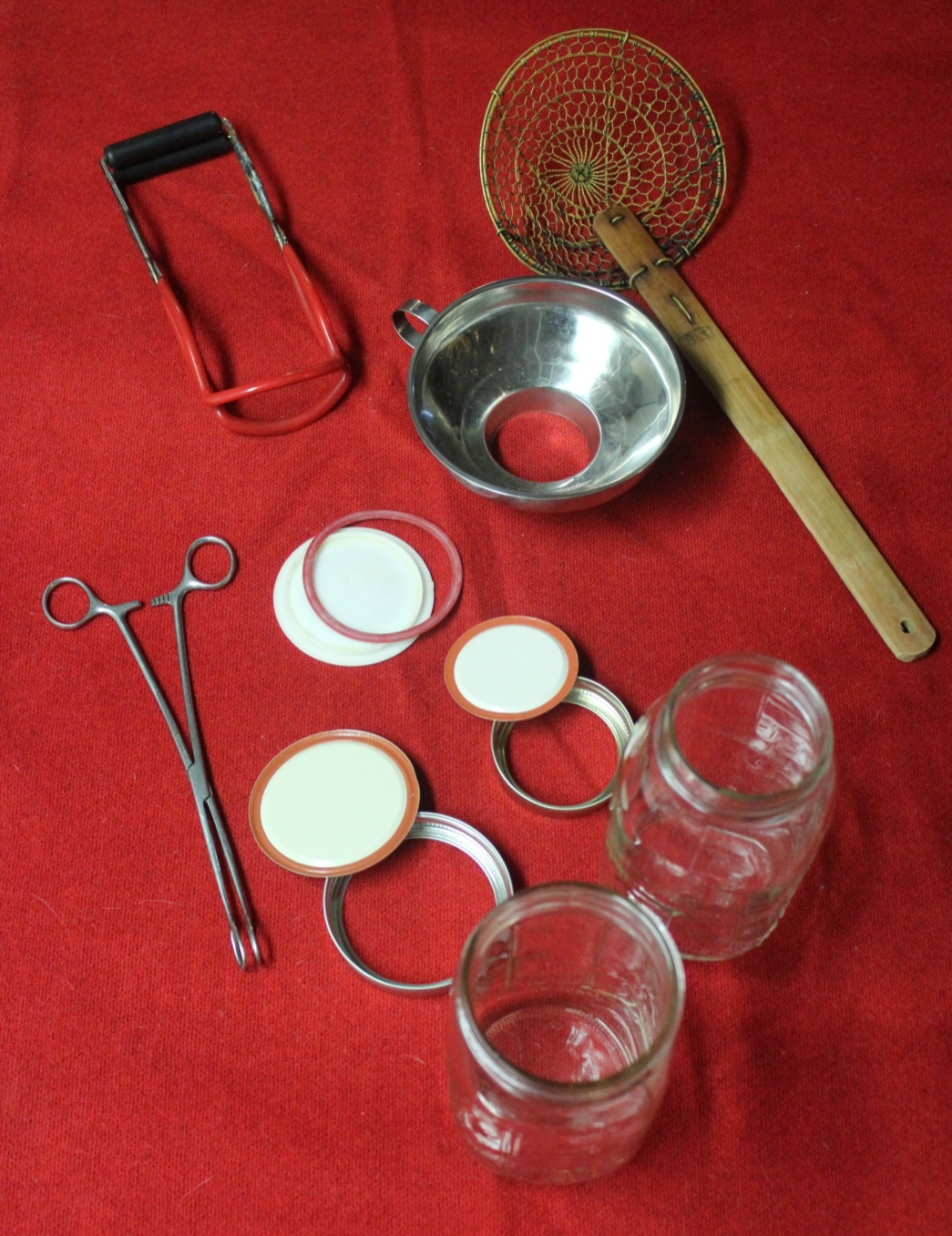 Photo of canning equipment including canning rings, lids, lid lifter, caning jar lifter, canning funnel and a skimmer for picking fruit out of hot water
